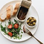 A gourmet Mediterranean dish featuring anchovies, olives, bread, and fresh salad on a plate.