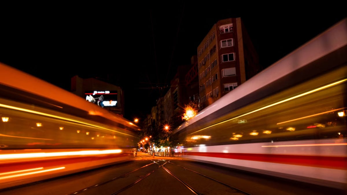 Twin trains speed past each other at night in a vibrant urban setting, creating a dynamic city atmosphere.